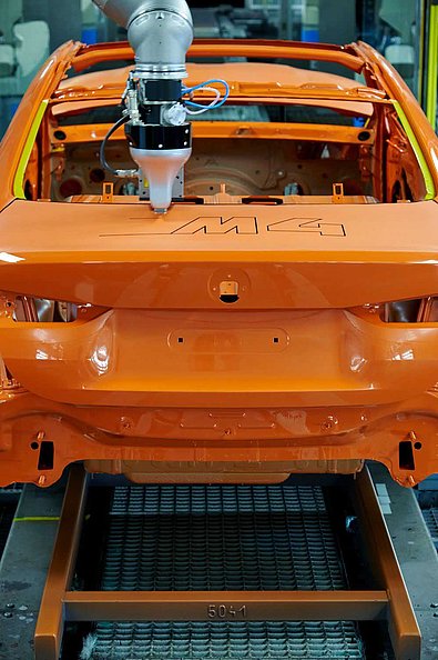 Robot starts applying a decor to the tailgate of an orange BMW M4