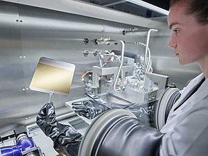 An einer SALD Anlage werden Versuche durchgeführt, eine Mitarbeiterin hält eine Beschichtungsprobe in einer Greifvorrichtung.