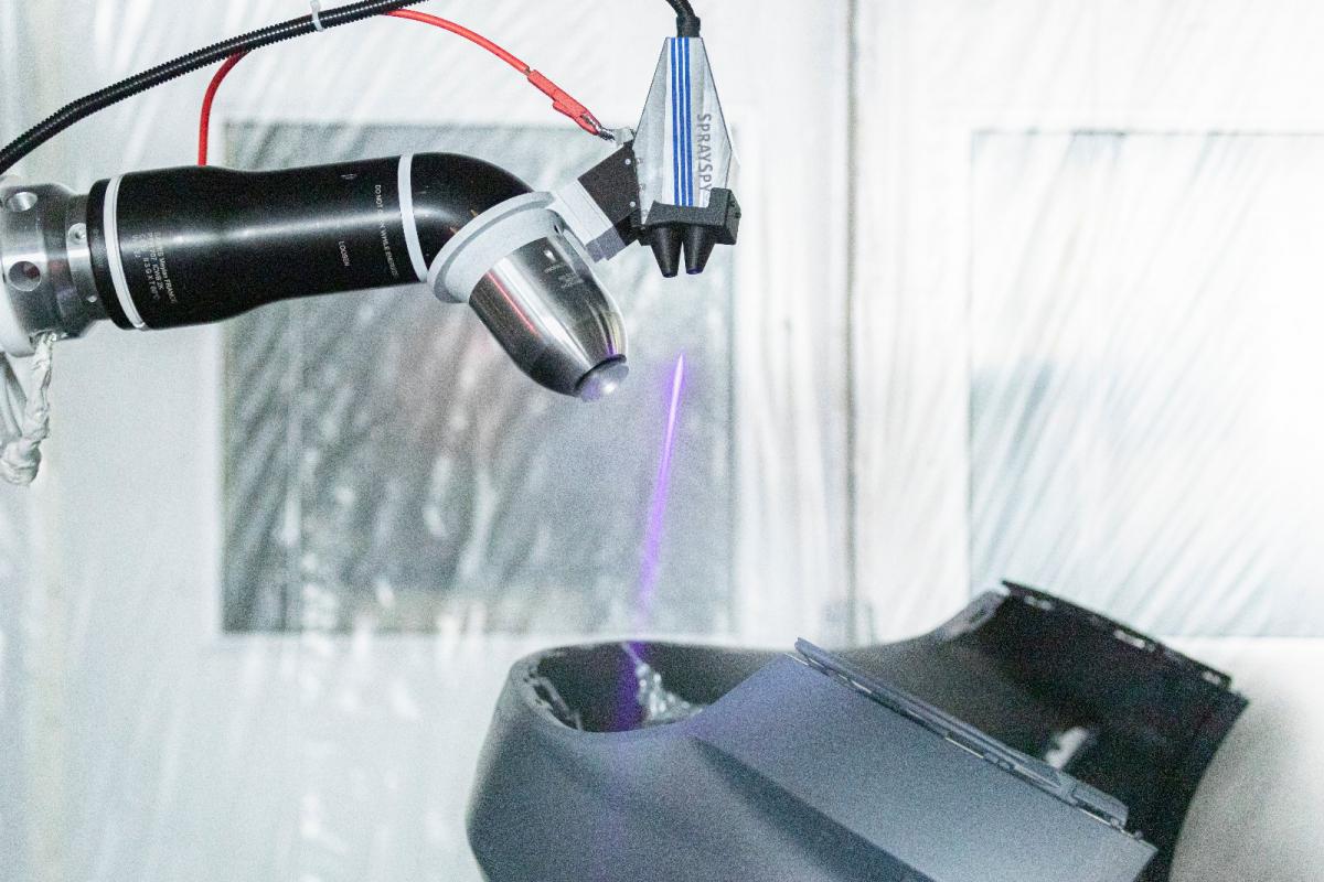 Ein Roboter sprüht Lack auf einen Stoßfänger und ein Inline-Laserdetektor sowie weitere Sensoren zeichnen alles auf.